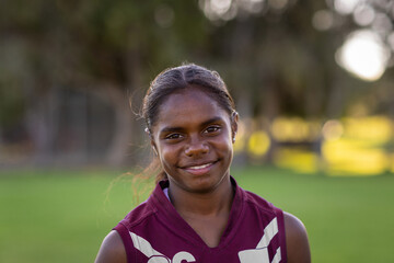 head and shoulders of aboriginal girl outdoors wearing footy shirt