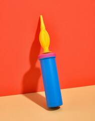 A hand air pump for blowing up birthday balloons blue and yellow color stands on the wall.