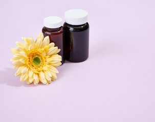 Two brown medical jars with different pills on a purple background. A bright yellow flower on the table. Copy space for text.