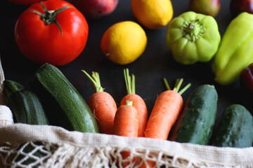 Mesh bag with fresh seasonal fruit and vegetable. Selective focus, dark background.