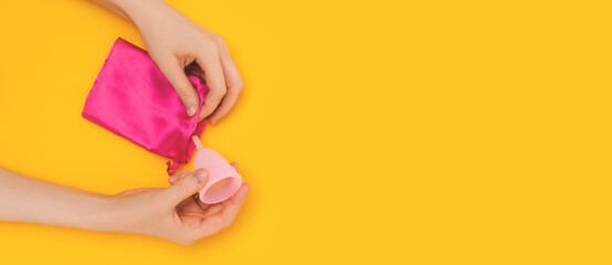 Banner with female hands take out the menstrual cup from the pink bag. Zero waste period concept on a yellow background. Place for text.