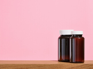 Two medical jars of brown pills for diseases, normal blood pressure on a pink background. Copy...
