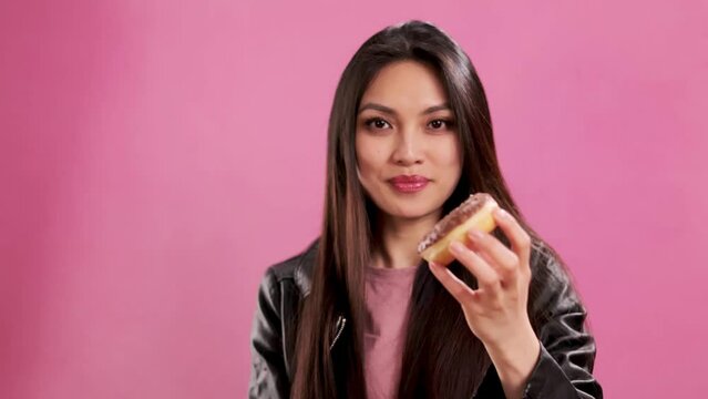Asian Girl with a confident smile in a studio eating donuts - extreme slow motion shot