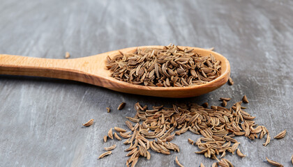 Side view on the light brown fragrant caraway spice seeds on the wooden spoon on the grey scratched background, horizontal format
