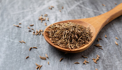 Side view on the light brown fragrant caraway spice seeds on the wooden spoon on the grey scratched...