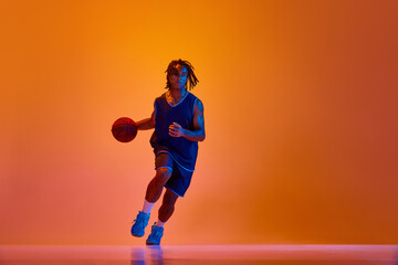 Fototapeta na wymiar Young athletic man, basketball player in motion during game, training against orange background in neon lights. Concept of professional sport, competition, hobby, game, competition, ad