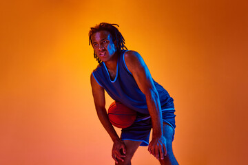 Competitive spirit. Young motivated man, athlete, basketball player standing with ball over orange...