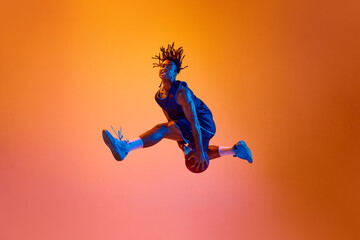 Slam dunk position. Athletic young man, basketball player in motion with ball against orange...