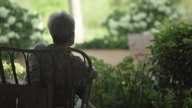 back of old elderly elder senior woman sitting resting relaxing on patio looking at garden