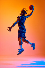 Full-length image of young sportsman, basketball player in motion, jumping with ball against orange background in neon lights. Concept of professional sport, competition, hobby, game, competition, ad