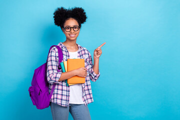 Portrait of diligent teenager with afro hairstyle wear plaid shirt hold book directing empty space isolated on blue color background