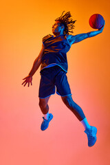 Fototapeta na wymiar Full-length image of young sportsman, basketball player in motion, jumping with ball against orange background in neon lights. Concept of professional sport, competition, hobby, game, competition, ad