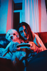 Close up portrait of A gamer or a streamer girl at home in a dark room with a game controller playing with her dog and sits in front of a monitor or TV.