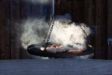 Grillen auf der Terrasse, Rauch über Bratwurst und Nackensteaks auf dem Schwenkgrill auf Holzfeuer...