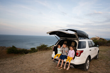 Three kids sitting in a car trunk on the beach by the sea. Cape Emine, Black sea coast, Bulgaria.
