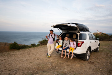 Family sitting on the back of a suv car at the beach against lighthouse. Cape Emine, Black sea...