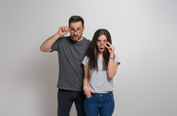 Amazed young couple with wide open eyes and mouth looking out eyeglasses at camera. Shocked man and woman dressed in casuals listening to unexpected news against background