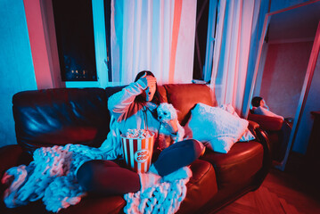 Close up portrait of Beautiful young girl hide her eyes watching movie at home in a dark room with a popcorn bucket playing with her dog and sits in front of a monitor or TV.