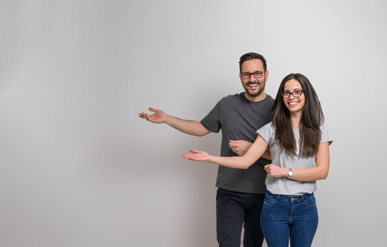 Portrait Of Cheerful Young Man And Woman Gesturing At Copy Space For Advertisement. Smiling Couple Wearing Eyeglasses Presenting Empty Space For Promotion Against Background