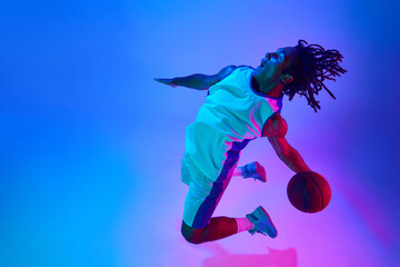 Dynamic image of professional basketball player in a jump with ball against gradient blue...