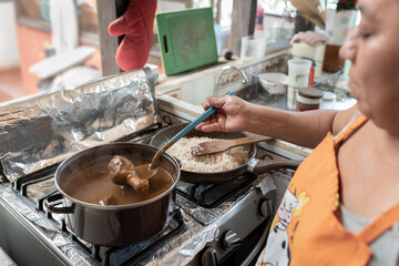 An adult Hispanic woman is boiling mole and fried chicken