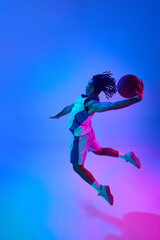 Fototapeta na wymiar Full-length image of young professional basketball player in motion, training, playing over gradient blue background in neon lights. Concept of professional sport, competition, game, competition, ad