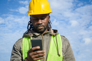young black man construction worker outdoors reading messages on phone