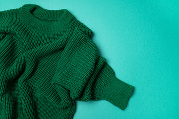 Green knitted sweater on paper green background top view copy space. Texture of woolen cotton winter autumn cozy sweater, clothes. Knitted jumper, pullover, fashion. Sweater close-up