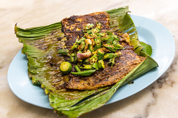 Grilled stingray fish with spices topped with okra vegetable on banana leaf popular food in Malaysia