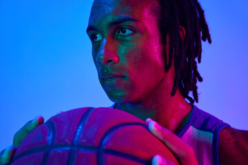 Portrait of handsome young man, basketball player posing with ball against gradient blue background...