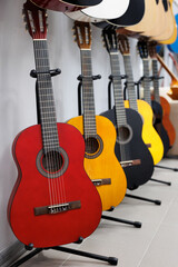 Fototapeta na wymiar Acoustic guitars of different sizes and colors on the stands in the musical instrument store