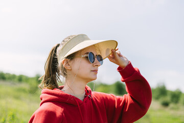 portrait of a young girl in a red hoodie with glasses and a cap against the sky