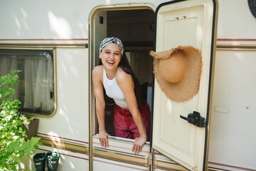 Happy hippie girl is having a good time in a camper trailer. Holiday, vacation, trip concept.