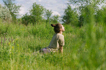 Naklejka na ściany i meble a young girl with a bun on her head in a T-shirt and leggings is doing yoga, doing stretching surrounded by nature