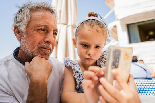 Grandfather and granddaughter taking selfie in cafe