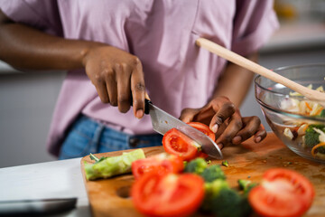 Young African woman in kitchen. Close up of woman making salad.