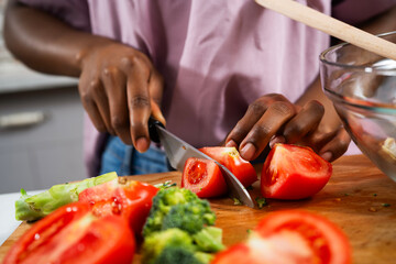 Young African woman in kitchen. Close up of woman making salad.