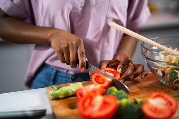 Young African woman in kitchen. Close up of woman making salad.