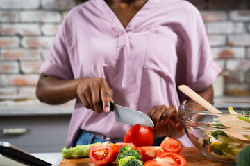 Young African woman in kitchen. Close up of woman making salad.