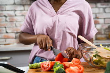 Young African woman in kitchen. Close up of woman making salad.