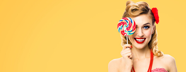 Image of excited woman with lollipop covering one eye. Pin up girl with happy smile. Retro style image. Orange yellow color background. Ophthalmology concept.