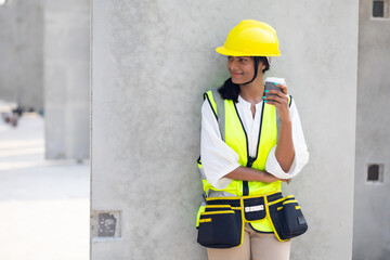 Happy indian female construction engineer wering safety hard hat helmet and drinking hot coffee at Heavy Industry Manufacturing Factory. Prefabricated concrete walls