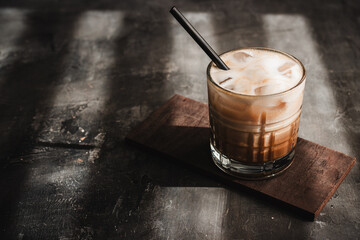 Ice latte coffee drink in a glass with a straw on dark background, summer refreshment drink