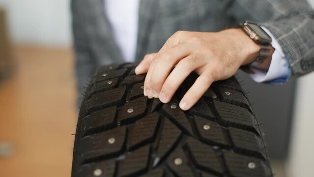 Closeup hands of unrecognizable buyer man checking and touching new winter tires with studs. Close up cropped shot of female client choosing studded tires for car in shop. Concept of ice on roads.
