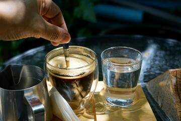 A hand was making with a spoon a hot coffee in a wooden tray on the tables in a cafe then soft sunlight.