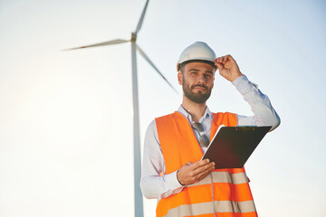 Black notepad in hands. Service engineer is on the field with windmills