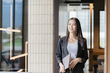 Fototapeta na wymiar Beautiful Asian businesswoman holding a laptop computer Walking smiling while walking into the office