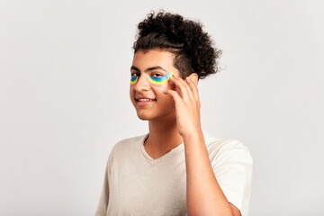 Portrait of young handsome guy with black curly hair applying hydrogel patches of rainbow color under his eyes. Swarthy smiling man practicing skincare to maintain his youthful and healthy appearance.