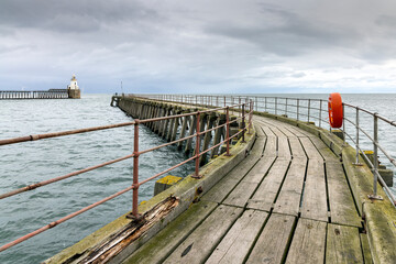 Fototapeta premium The old wooden south pier at the entrance to the Port of Blyth in Northumberland, with the lighthouse on the north pier in the distance.