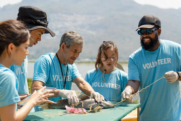 team of volunteers pulling trash out of dead fish mouth, impact of plastic pollution in ocean,...